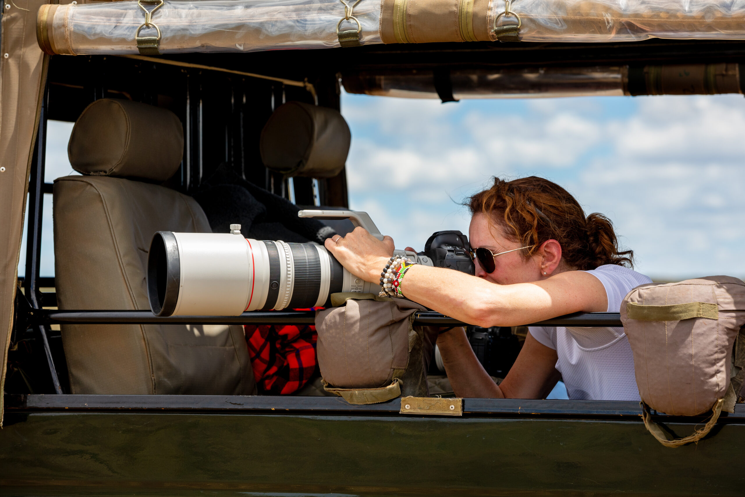 Wildlife photographer taking pictures of animals during a safari from an open jeep using a telephoto camera lens.